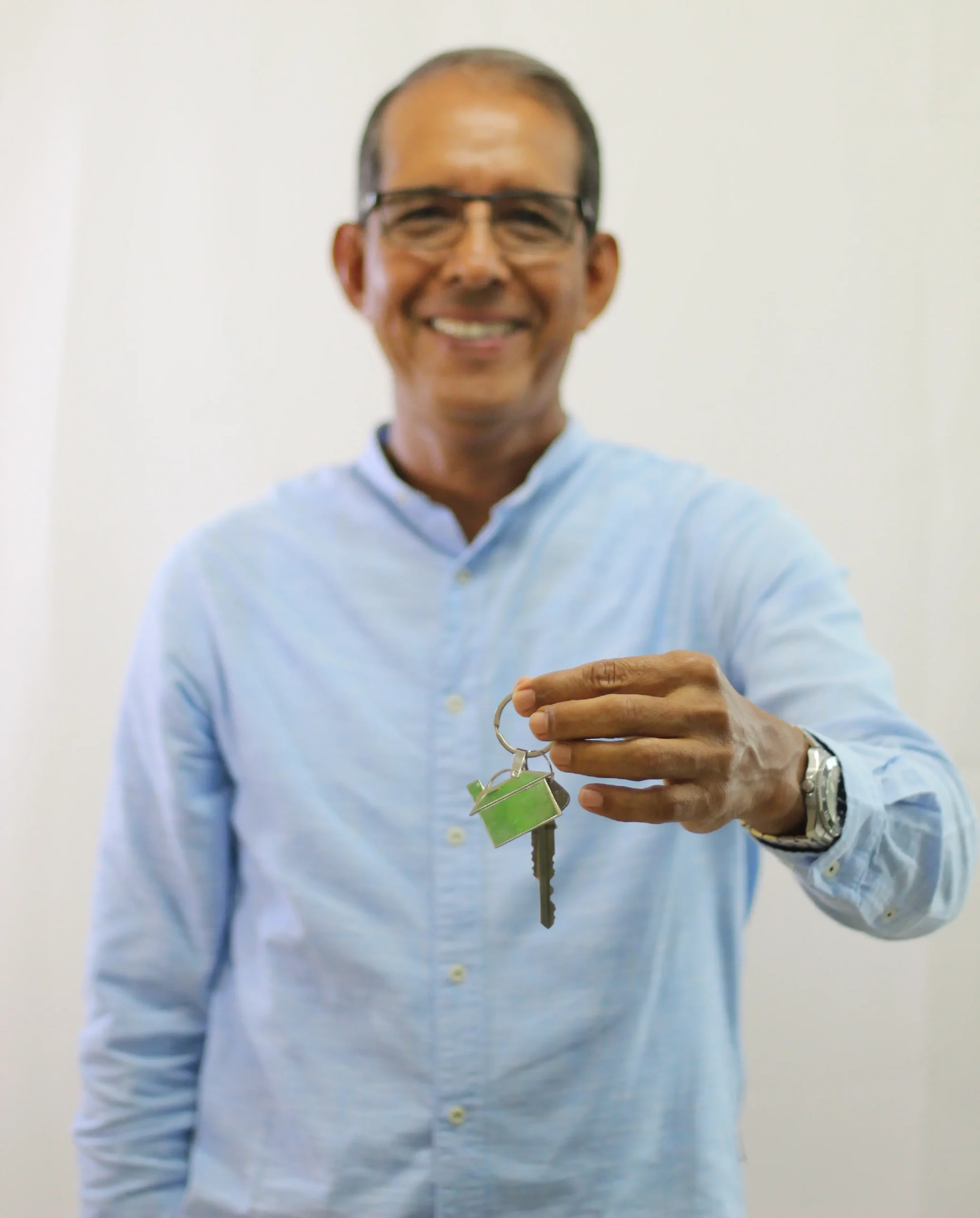 Hombre sonriente con camisa azul sostiene unas llaves, simbolizando la entrega de una propiedad en Veracruz.